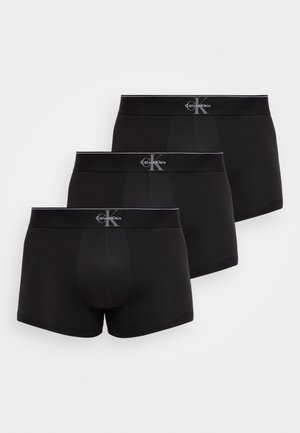 Tre svarte Calvin Klein-bokserbriefs med merkede midjebånd arrangert i en trinnvis formasjon på en hvit bakgrunn.