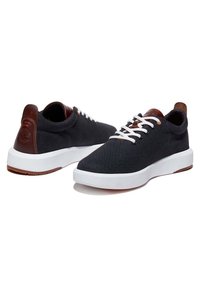 Baskets en toile noire avec lacets blancs, accents en cuir marron au talon et semelle en caoutchouc blanche. Présentent un design simple et épuré.