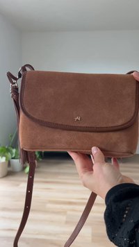 Bruine suede schoudertas met een flapsluiting, gouden logo-detail en een afneembare verstelbare strap met een franjesaccent.