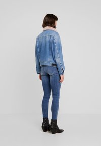 Giacca di denim azzurro chiaro con colletto in shearling rosa, dal design corto e maniche con bottoni, abbinata a jeans skinny blu scuro.