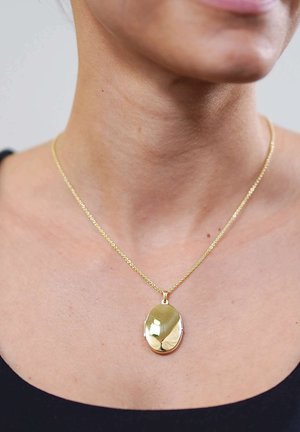 Close-up of a gold oval locket pendant on a fine chain worn around a person's neck against a black top background.