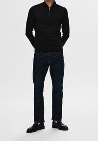 Czarny pulower na zamek, długie rękawy, dopasowany krój. Zestawiony z ciemnoniebieskimi jeansami i czarnymi mokasynami. Prosta, fakturowana tkanina tworzy ładny kontrast.