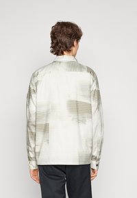 Camisa de manga larga en gris claro con un patrón de cuadros, que presenta un cuello recto y una tapeta de botones, fabricada con una tela suave y brillante.