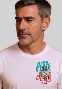 Witte t-shirt met korte mouwen, voorzien van een kleurrijke "Pizza Club" graphic met pizzastukken en tekst in turquoise en rode accenten.