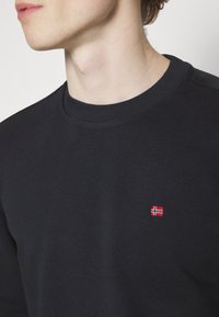 Felpa nera con girocollo in tessuto morbido, con una piccola bandiera norvegese ricamata in rosso e bianco sul petto a sinistra.