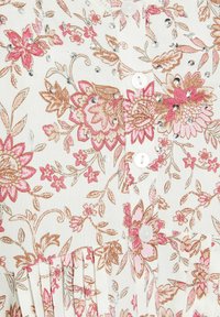 Blusa floral de tela blanca con estampados de flores en rosa y marrón, adornada con rhinestones. Presenta un cierre de botones y un dobladillo plisado.