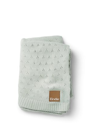 Copertina per neonati lavorata a maglia di colore verde chiaro con un piccolo motivo a occhiello e una toppa in pelle marrone con l'etichetta "Elodie" su sfondo bianco.