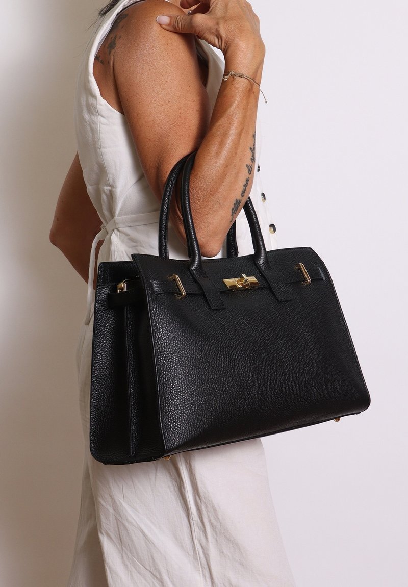 Zwarte leren handtas met een gestructureerde afwerking, strakke vorm, dubbele handvaten en gouden hardware accenten. Voorzien van een sluiting met een klipsluiting aan de voorkant.
