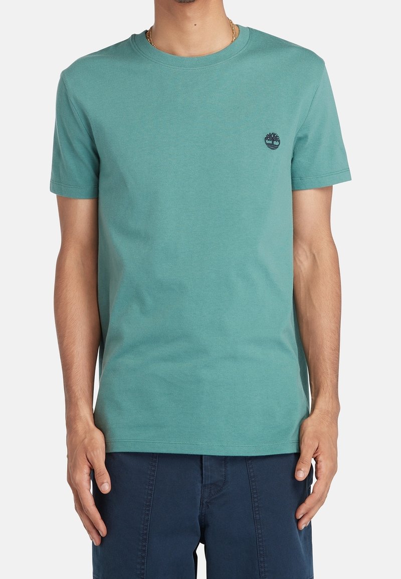 T-shirt à manches courtes en teal en coton. Il présente un col rond et un petit logo brodé sur la poitrine. Design simple, sans motifs.
