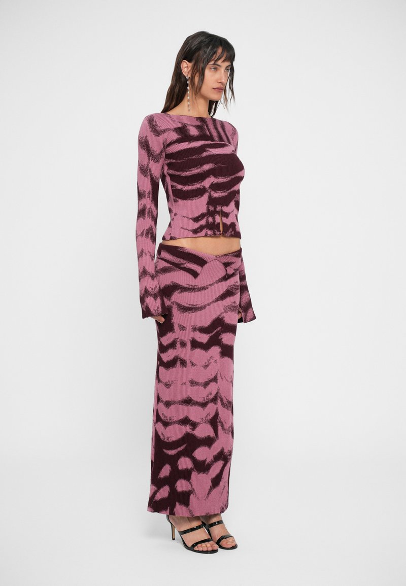 Strick-Set bestehend aus einem verkürzten Langarmoberteil und einem bodenlangen Rock in Pink mit dunkellila abstrakten Wellenmustern.