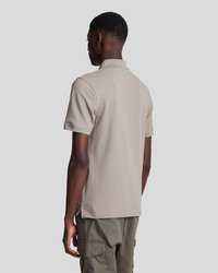 Polo de manga corta color beige, hecho de algodón suave, que cuenta con un cuello clásico y aberturas en los lados del dobladillo. Combinado con pantalones cargo.