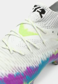 White soccer shoe with a gradient pattern in pink, blue, and green. Features a textured upper, standard laces, and a high sock-like collar.