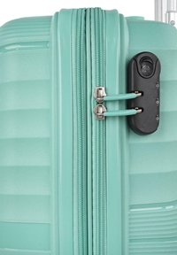Maleta rígida de color verde menta con estrías horizontales, dos cremalleras plateadas y un candado de combinación negro en el lateral.