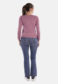 Top viola a maniche lunghe abbinato a jeans a zampa d'elefante blu. Il top ha un design aderente, mentre i jeans presentano un leggero sbiadimento e tasche posteriori.