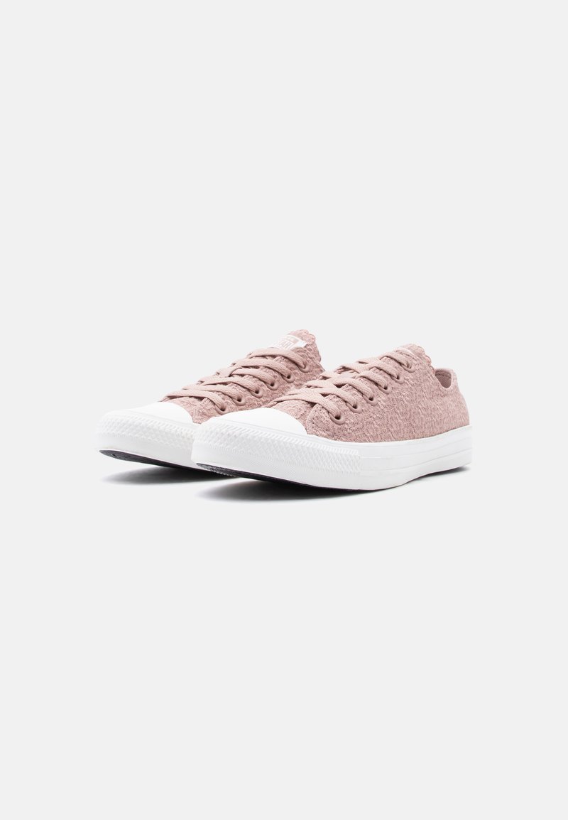 Paar flacher Schnürsneaker in staubigem Rosa mit weißen Gummikappen an der Zehenpartie und weißen Sohlen, vor einem schlichten hellgrauen Hintergrund.