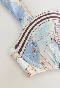 Gros plan d'un haut de bikini avec un imprimé carte du monde et des bandes marron le long des bords sur un tissu clair.