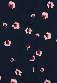 Tessuto blu navy con motivi floreali sparsi in rosa chiaro e rosso scuro. Tre bottoni neri sono visibili lungo il centro.