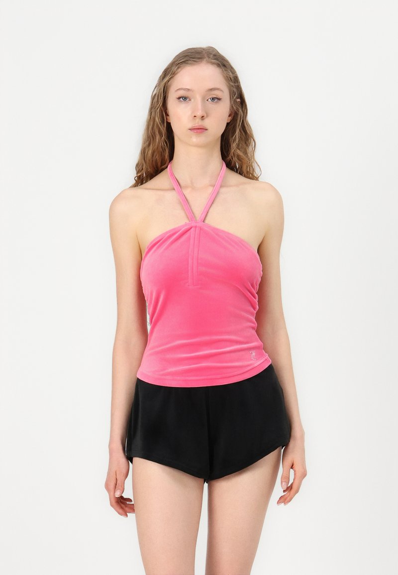 Ροζ βελούδινη τοπ με halter και πτυχές μπροστά, συνδυασμένη με μαύρα ψηλόμεσα σορτς. Το ύφασμα φαίνεται μαλακό με λεία υφή.