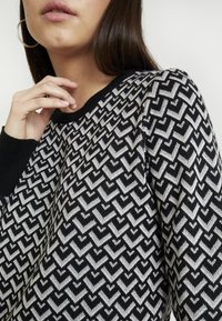 Maglione nero lavorato a maglia con un motivo a zigzag argentato, colletto rotondo a coste e maniche lunghe con polsini neri.