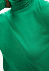 Grön polo tröja i mjukt, stretchigt material. Den har en figurnära design med en slät yta och en subtil lyster.