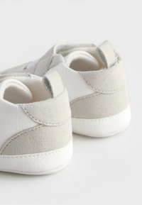 Baskets blanches et gris clair avec une finition en cuir lisse et des accents en velours. Capuchon de talon rond et détails de couture contrastants visibles.
