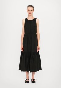 Black, sleeveless dress with a high neckline, fitted bodice, and flared, tiered skirt. Made of smooth fabric with a subtle sheen.
