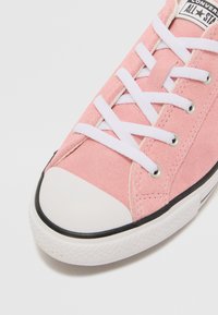 Helle rosa Wildleder-Sneaker mit weißen Schnürsenkeln, Gummikappen und schwarzem Sohlenrand. Verfügt über runde Ösen und ein „All Star“-Logo auf der Zunge.