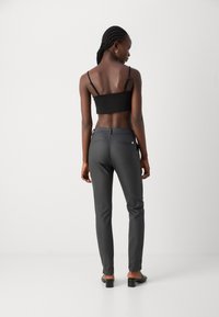 Schwarzes Crop-Top und schlanke graue Hose aus glattem Stoff, mit zwei Gesäßtaschen und einem kleinen Logo-Detail auf der rechten Seite.