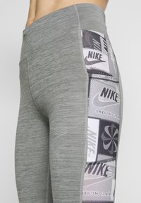Leggings sportivi grigi con un tessuto testurizzato, dotati di un pannello laterale con grafiche in bianco e nero, comprese loghi e motivi.