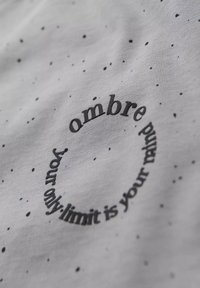 Tela de color gris claro con un patrón moteado. Texto circular en negro que dice: "el único límite eres tú mismo". Textura suave, parecida al algodón.