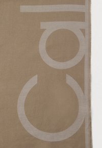 Beige stof med store, delvist synlige lysegrå geometriske former og en let frynsed kant på højre side.