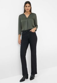 Blusa verde scuro con scollatura a V e maniche lunghe abbinata a jeans neri a gamba dritta e stivali neri con tacco. Tessuto liscio con dettagli minimi.