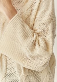 Adīts krēms džemperis ar dažādu aušanas struktūru, ieskaitot kabeli un atvērtu austi, ar platām ribotām piedurknēm un mīkstu, brīvu piegriezumu.