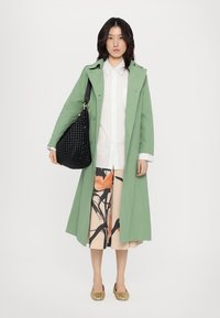 Heled roheline trench-kate, valge nööbiga särk, lillemustriga midi-seelik, must punutud kott ja kuldsed sisetallad. Minimalistlik disain ja pehmed tekstuurid.