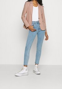 Světle růžový blazer, bílý top bez rukávů, světle modré skinny džíny a bílé vysoké tenisky. Blazer má jedno tlačítko a má volný střih.