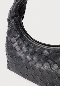 Mustat kudotut nahkakäsilaukut, joissa on kaareva kahva ja hopeanvärinen vetoketju yläosassa, taustan ollessa yksinkertainen.