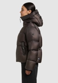 Pehme ja tumedat pruunist kapuutsiga jope, millel on vertikaalne tikandmuster, küljetaskud ning must logomärk varrukal.