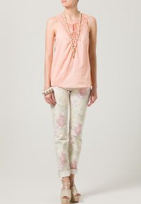 Peach sleeveless blouse with lace neckline, paired with light floral-patterned pants. Model wears beige platform sandals and a beaded bracelet.