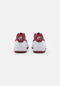Nike Air sneakers feature a white leather upper with red accents, rounded shape, padded collar, and textured rubber sole.