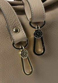 Bolso de mano de cuero beige en primer plano, con dos clips dorados, una correa texturizada y una superficie lisa con costuras en contraste.