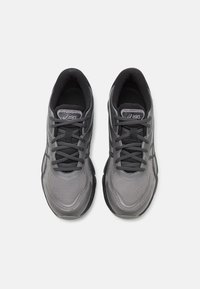 Gray athletic shoes featuring a mesh upper, padded tongue, laces, and a thick rubber outsole with subtle design accents.