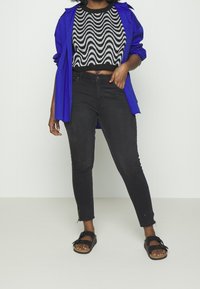 Suéter negro corto con patrón de olas, camisa azul oversized, jeans negros ajustados y sandalias negras con hebilla decorativa.