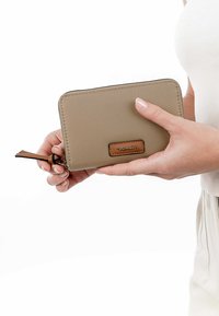 Beige Brieftasche aus strukturiertem Material, mit einem braunen Akzentlabel, Reißverschluss und einem Handgelenkband für einfachen Transport.