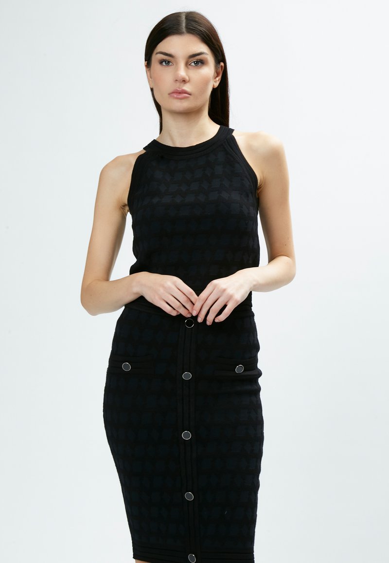 Abito nero a maglia con silhouette aderente, design senza maniche e finitura testurizzata. Presenta due tasche frontali e bottoni circolari lungo la parte anteriore.