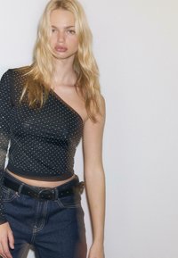 Crni top s jednim ramenom sa srebrnim ukrasima, glatke teksture. Nosile su se s hlačama od tamnog denima visokog struka i crnim pojasom.