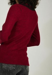 Czerwona bluzka z długim rękawem wykonana z teksturowanej dzianiny, z kontrastowym czarnym dekoltem, dopasowanym krojem i widocznymi detalami szwów.