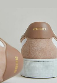 Brūni zamšādas kedu ar baltu ādas paneli, apaļu formu un teksturētu baltu gumijas zoli. Zelta "REISS" logo uz papēža.