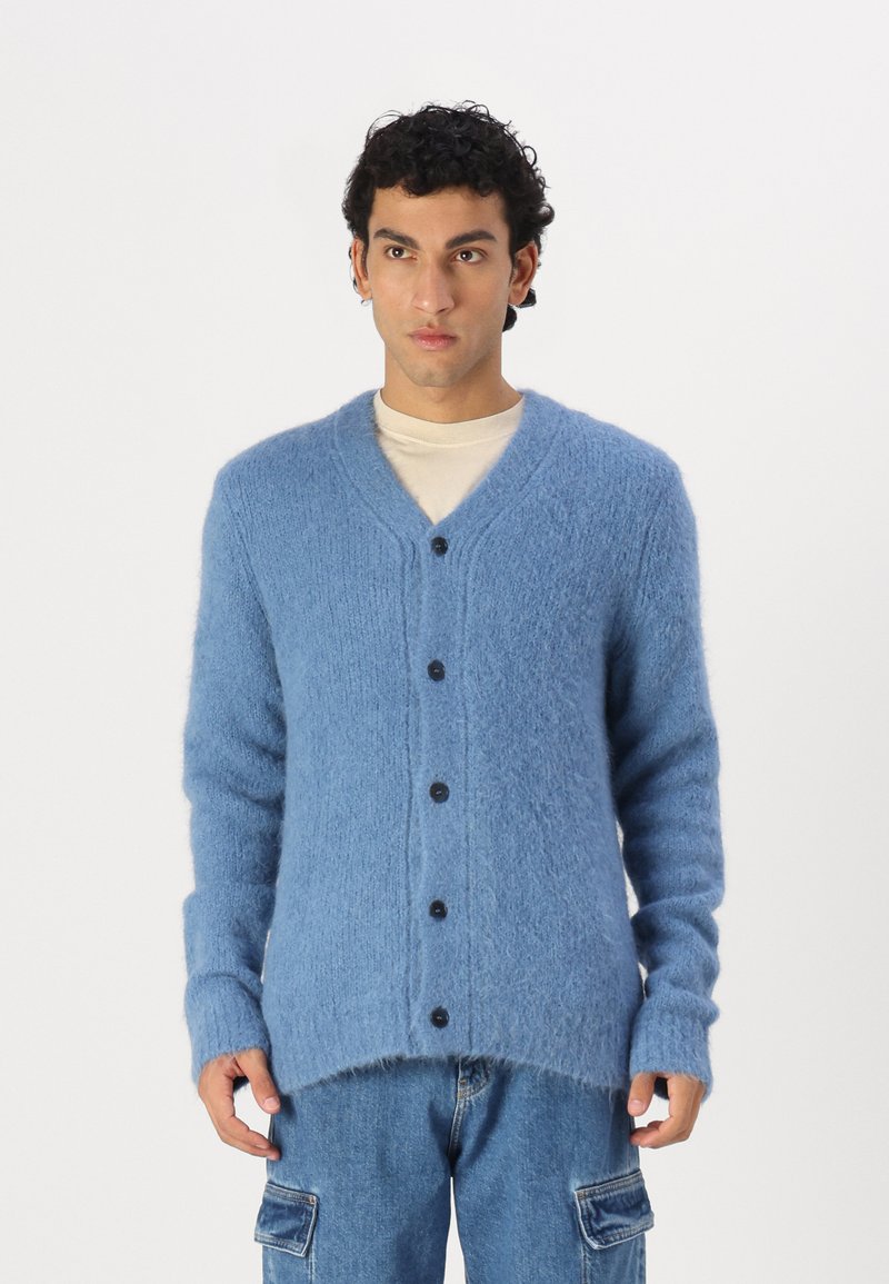 Μπλε, χνουδωτό καζάκι από μαλακό υλικό με V ντεκολτέ, μακριά μανίκια και έξι μαύρα κουμπιά μπροστά. Οι άκρες είναι ελαφρώς φθαρμένες.