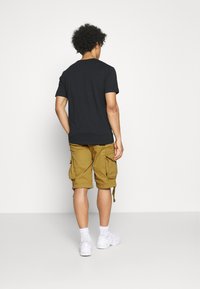 Svart T-skjorte og khaki cargo-shorts med flere lommer. Joggesko og hvite sokker synlige. Enkel design, avslappet passform.