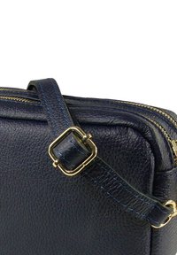 Donkerblauwe leren crossbodytas met een gestructureerd oppervlak, gouden hardware en een blauw gestikte riem. Voorzien van een ritssluiting aan de bovenkant.